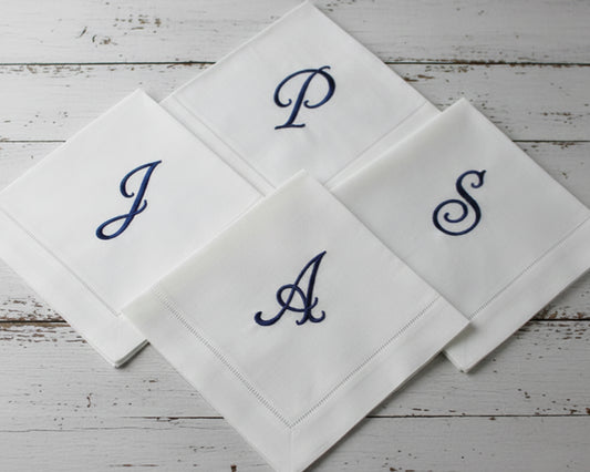 Custom embroidered white hemstitch napkin featuring a detailed green heraldic shield crest with a lion, mountain motif, and 'R' monogram