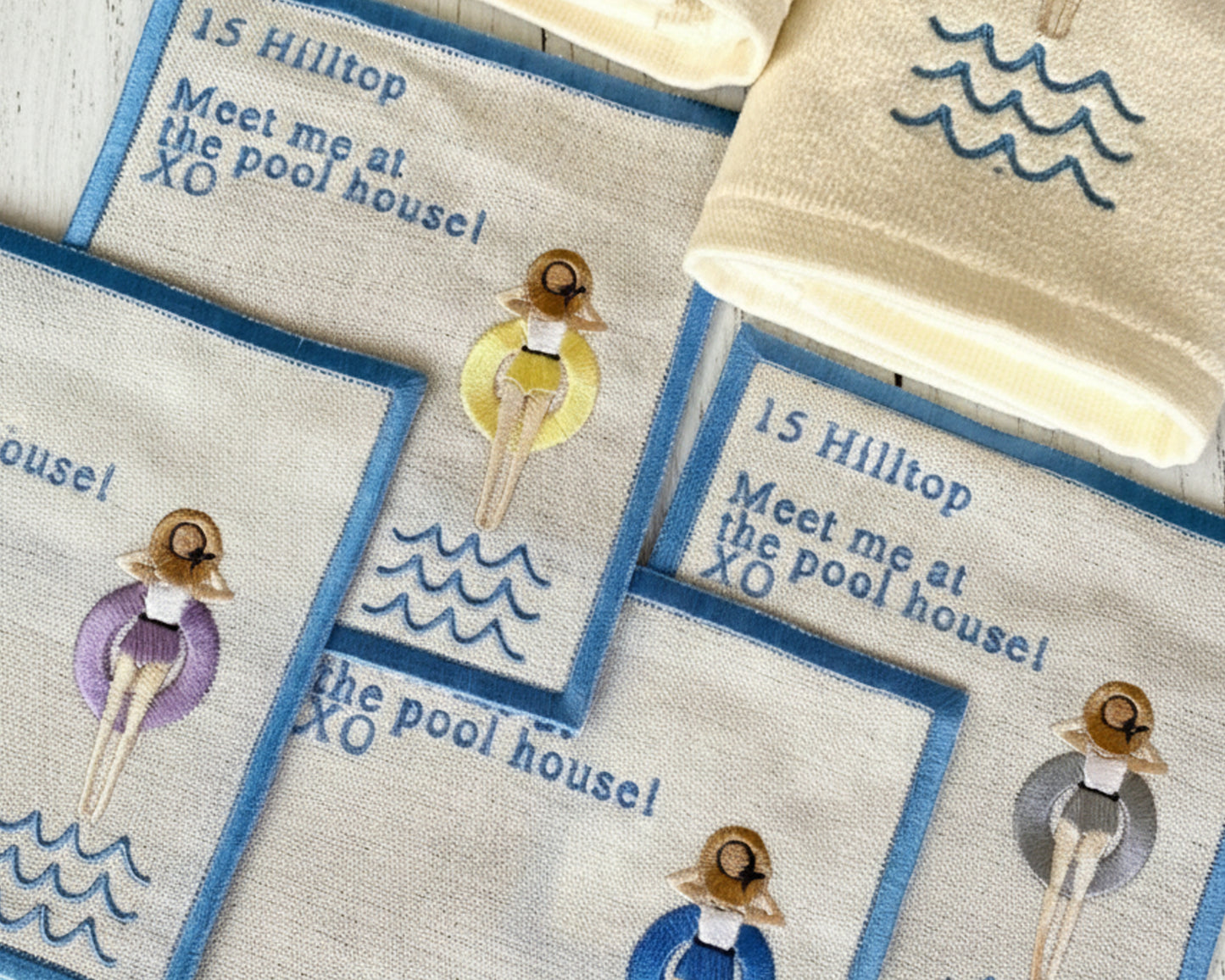 Close-up detail of high-density embroidery showing sun-loungers in orange and purple floaties on premium linen.