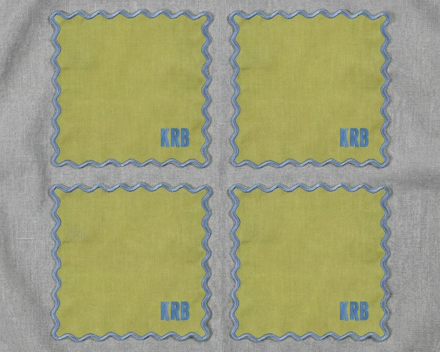 A close-up of four navy blue linen napkins with white scalloped borders, highlighting the premium fabric texture and wave stitching.