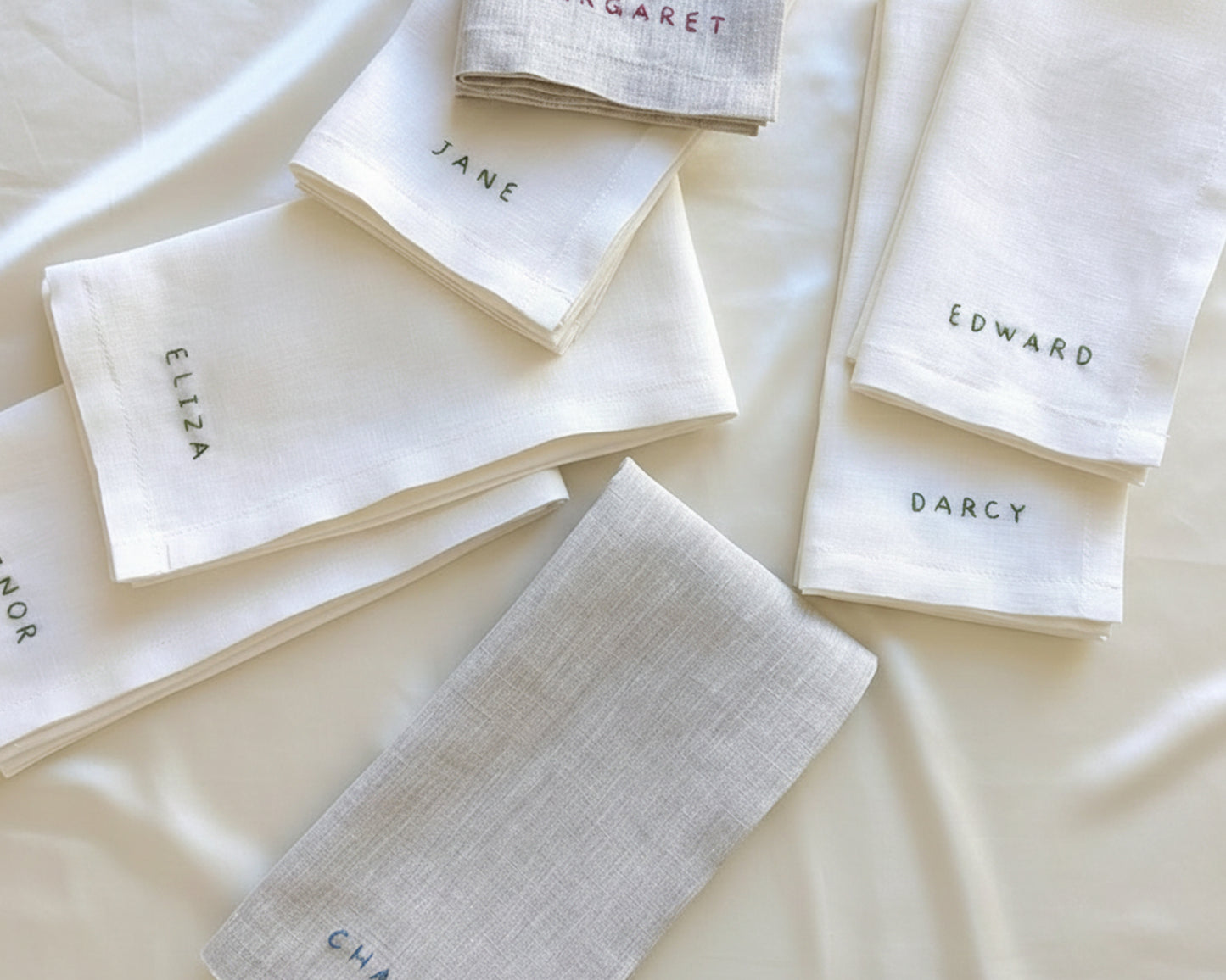A collection of six white cotton napkins featuring machine-calibrated hemstitch borders and uniform name embroidery in a digital script font.