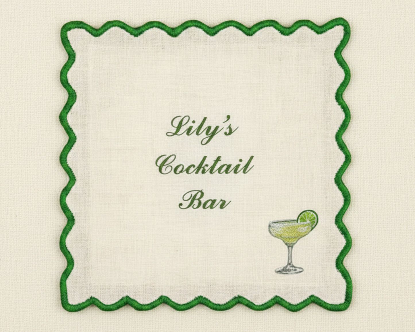 A white cotton bar napkin featuring a vibrant green scalloped border and a custom embroidered margarita glass with a lime garnish.