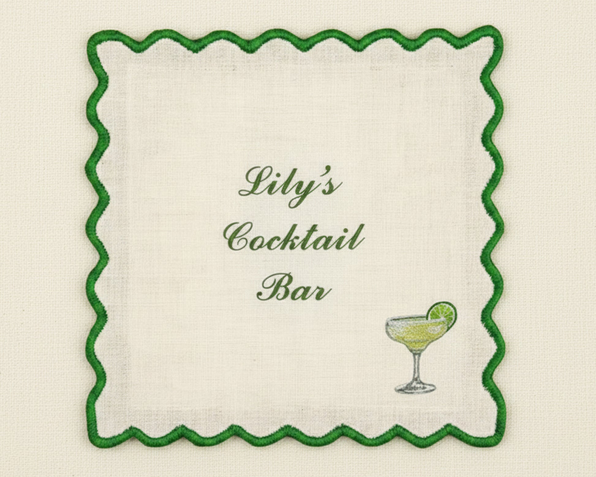 A white cotton bar napkin featuring a vibrant green scalloped border and a custom embroidered margarita glass with a lime garnish.