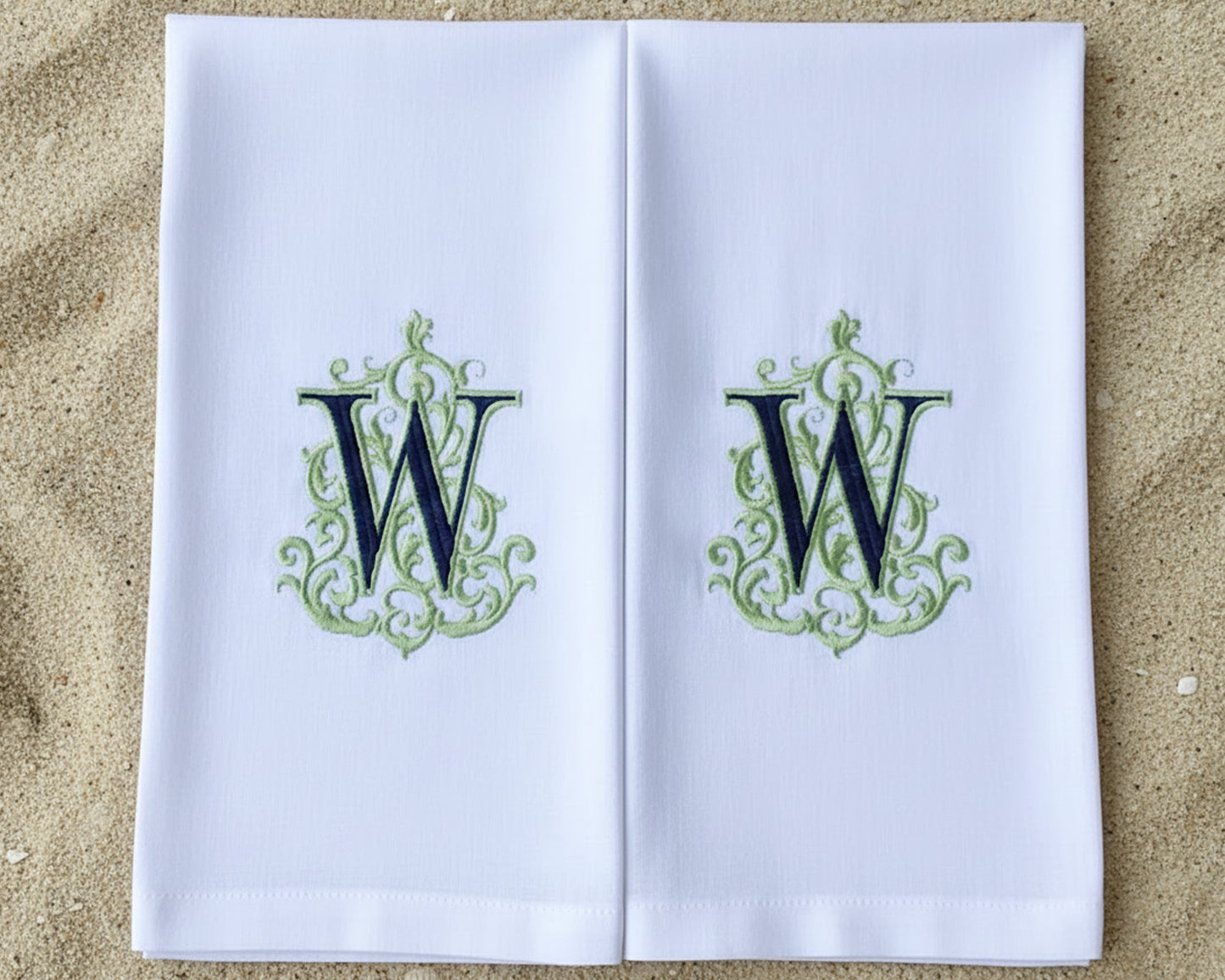 A set of matching white cotton napkins: one large dinner napkin and one small cocktail napkin with green monograms