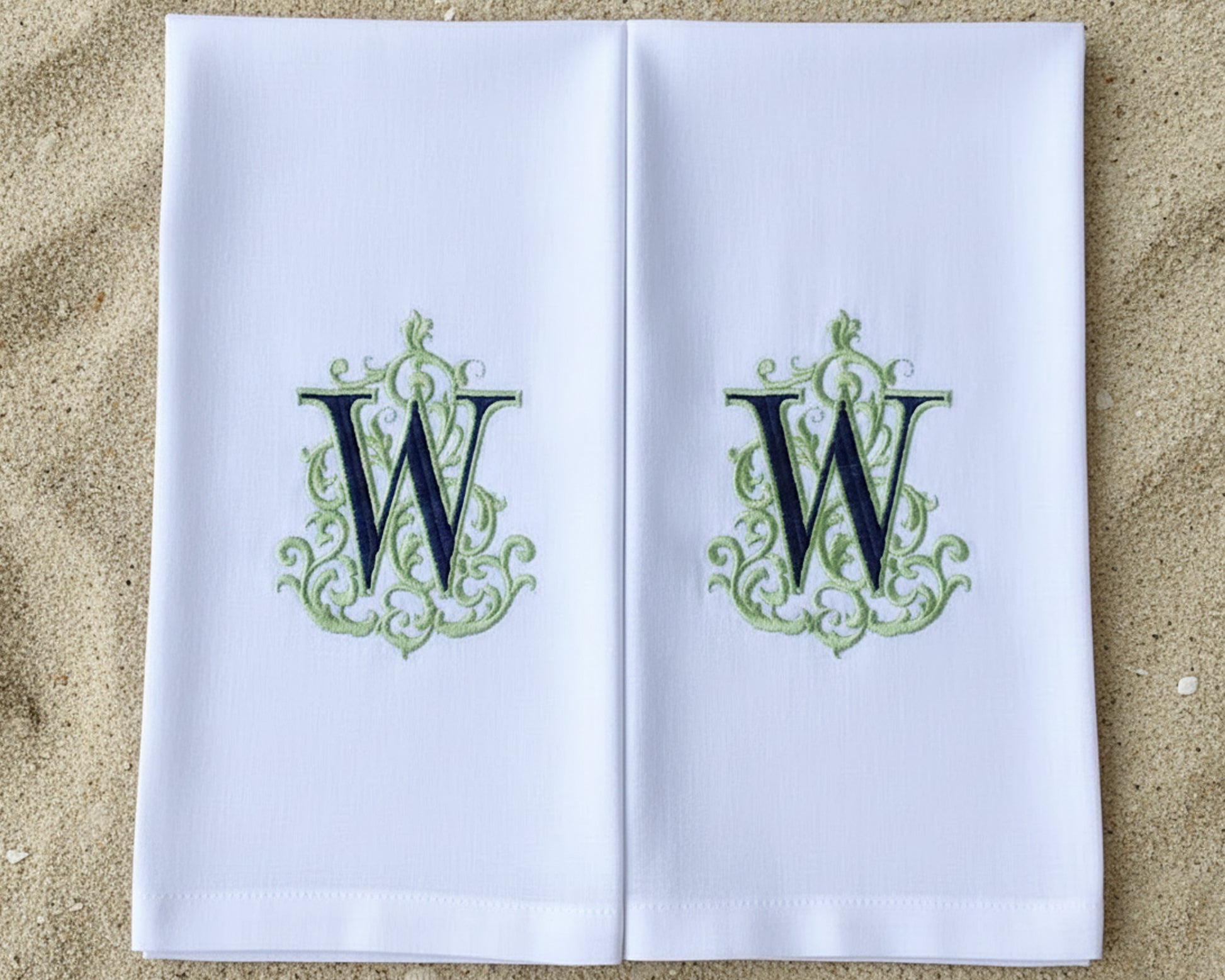 A set of matching white cotton napkins: one large dinner napkin and one small cocktail napkin with green monograms