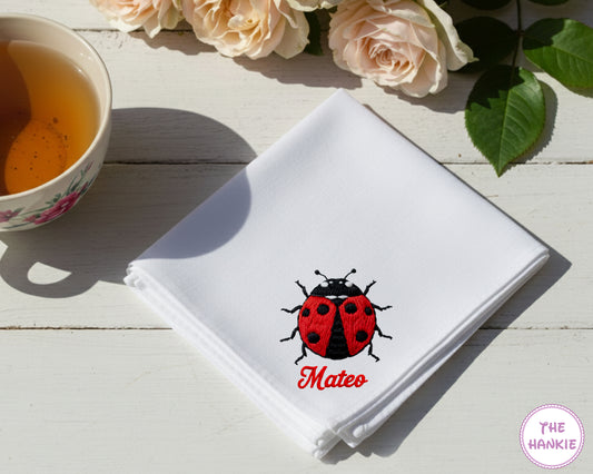 A crisp white cotton handkerchief personalized with the name "Mateo" in red script and a vibrant red-and-black embroidered ladybug.