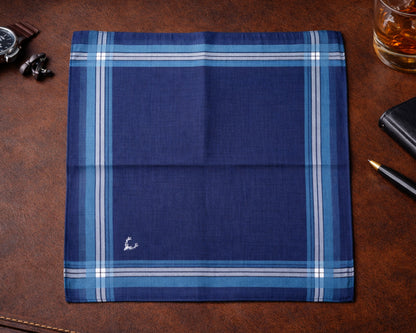 Folded blue plaid fabric on a brown leather surface with a glass of whiskey and accessories.