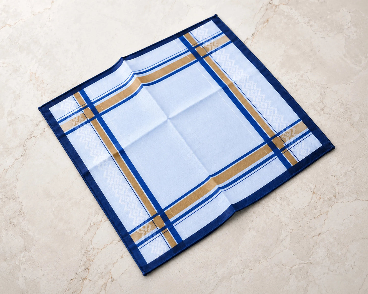 Folded fabric with blue and gold plaid pattern on a beige surface