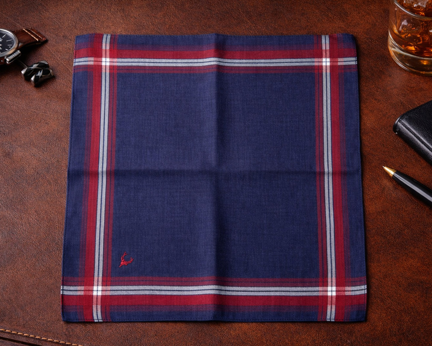 Folded dark purple plaid fabric on a brown leather surface with a glass of whiskey and accessories.