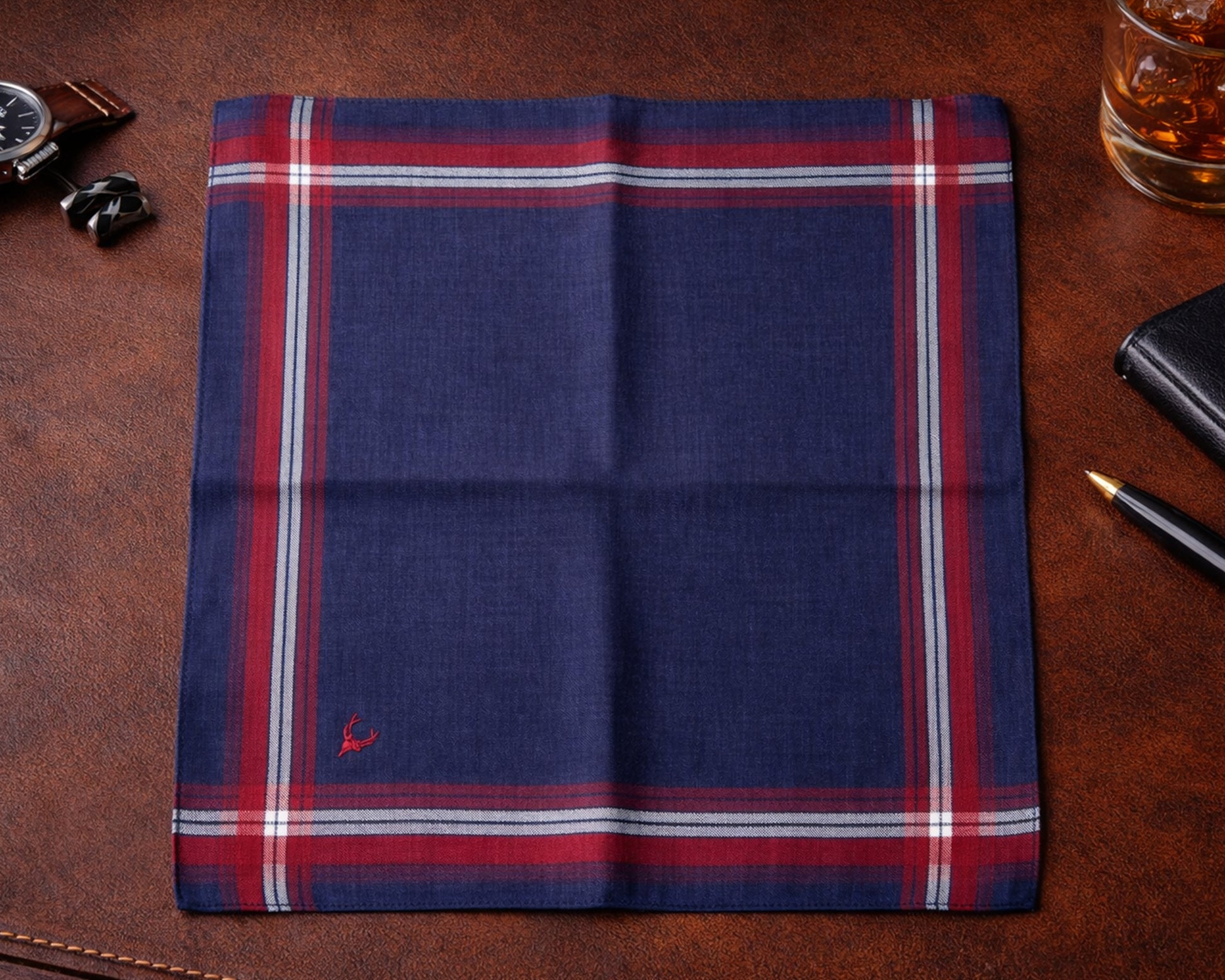 Folded dark purple plaid fabric on a brown leather surface with a glass of whiskey and accessories.