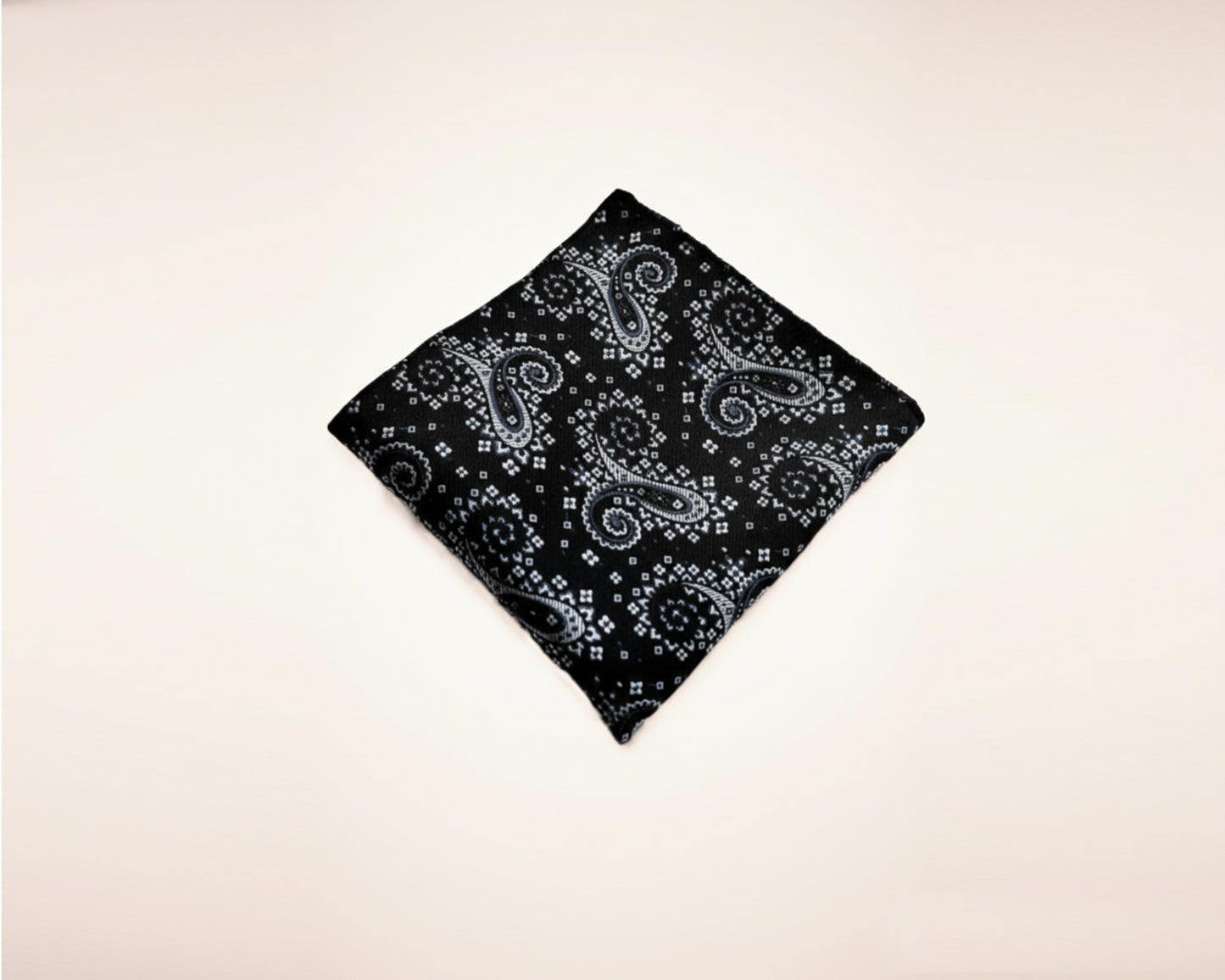 Flat lay view of a folded midnight onyx and silver paisley cotton handkerchief for men on a white background.