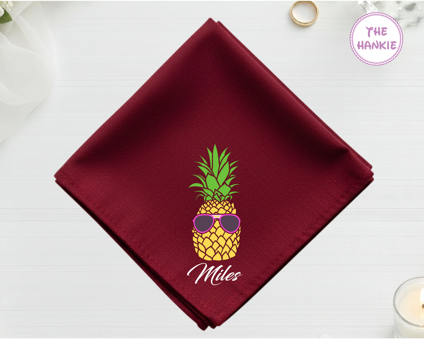 A rich cranberry red cotton handkerchief customized with the name "Miles" and a detailed pineapple with pink sunglasses.