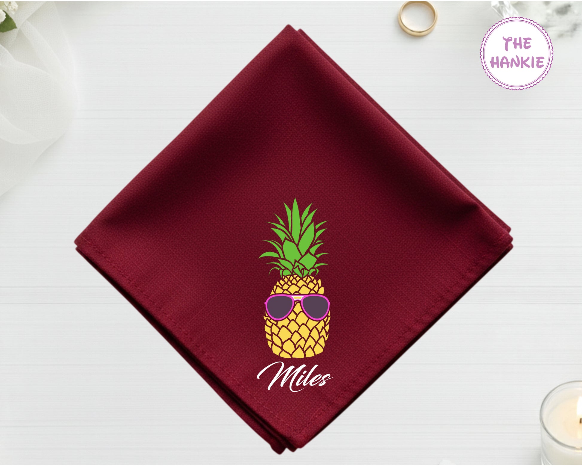 A rich cranberry red cotton handkerchief customized with the name "Miles" and a detailed pineapple with pink sunglasses.
