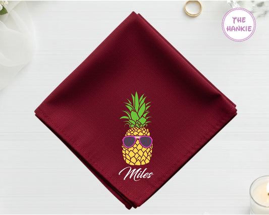 A rich cranberry red cotton handkerchief customized with the name "Miles" and a detailed pineapple with pink sunglasses.