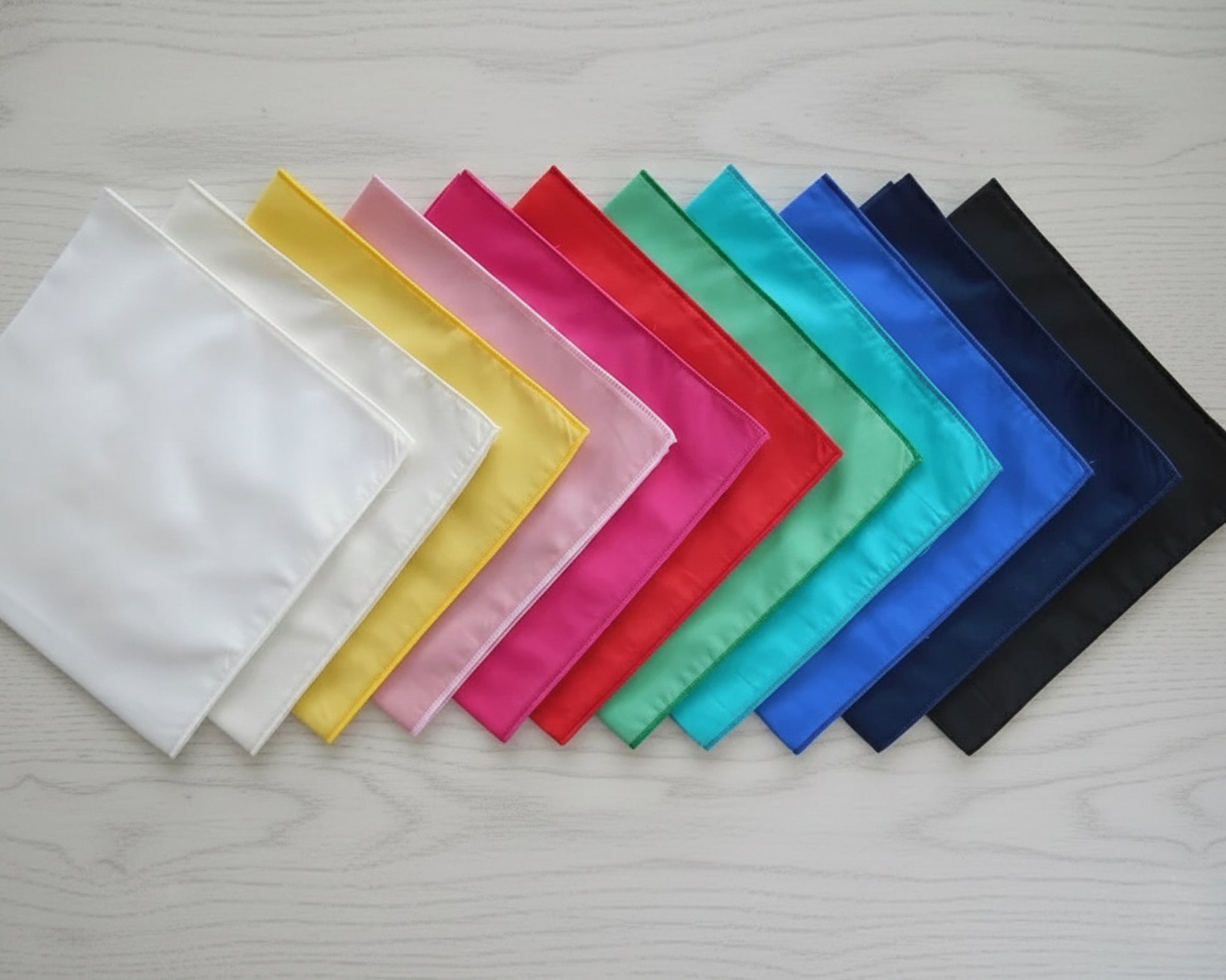 A minimalist stack of three pure cotton handkerchiefs in crisp white, soft cream, and bright yellow.