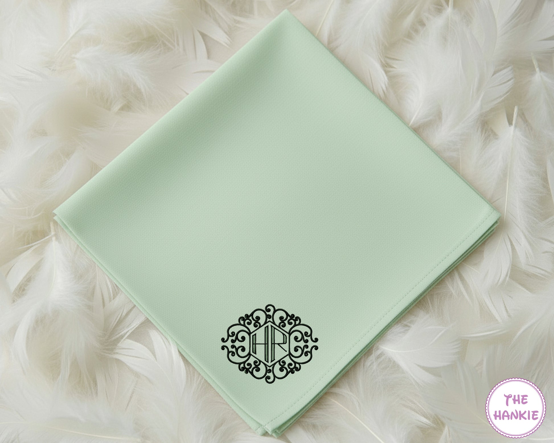 A mint green 100% cotton handkerchief showcasing a bold, black circular crest monogram with the initials "HRC".