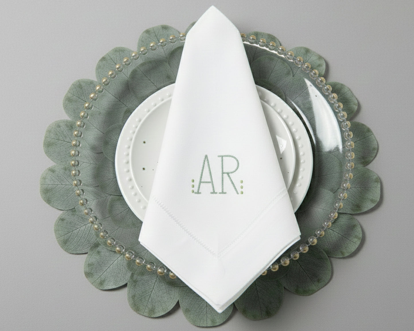 Personalized white dinner napkin with a minimalist sage green 'AR' monogram and hemstitch border detail