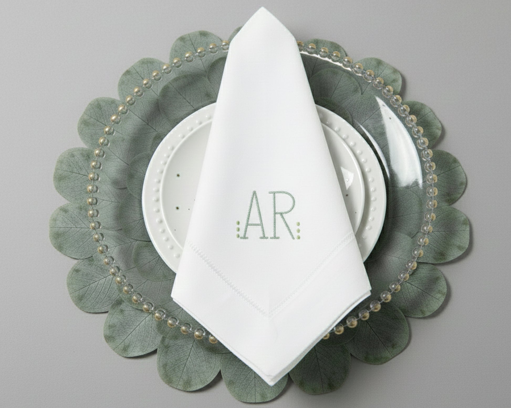 Personalized white dinner napkin with a minimalist sage green 'AR' monogram and hemstitch border detail