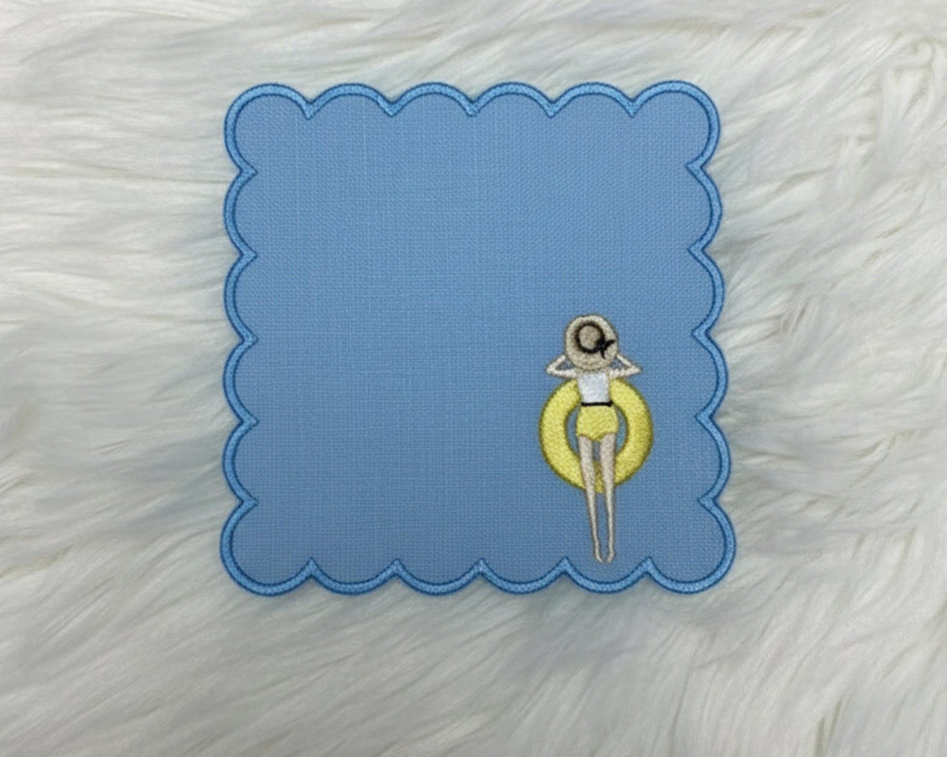 A row of four white linen cocktail napkins with blue borders, each featuring a girl in a different colored floaty: pink, yellow, orange, and purple.