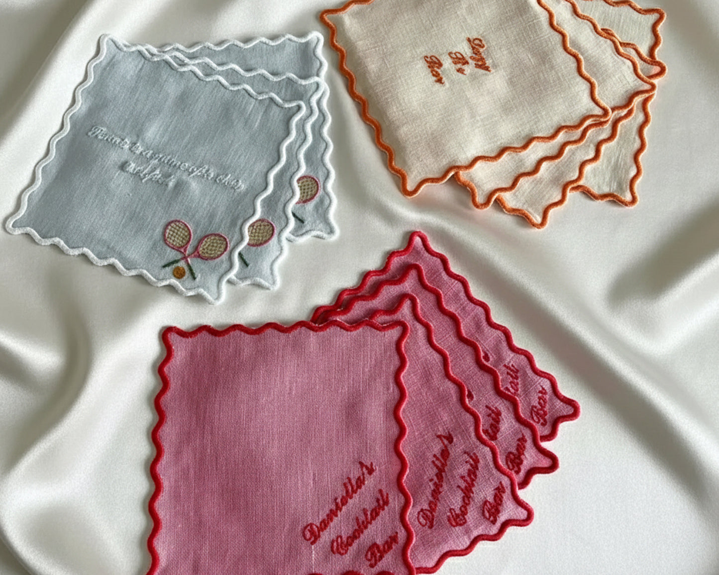 A light blue scalloped-edge cotton coaster featuring white embroidered text for "Natalie’s Cocktail Bar" and a minimalist poodle line-art icon.