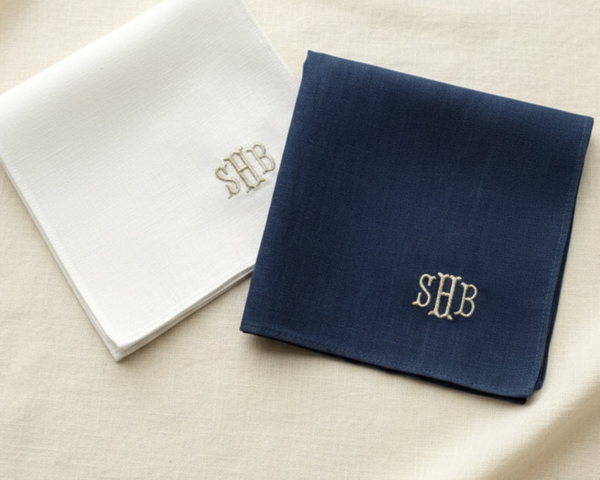 A white and a navy blue linen pocket square with "SHB" monogrammed embroidery.