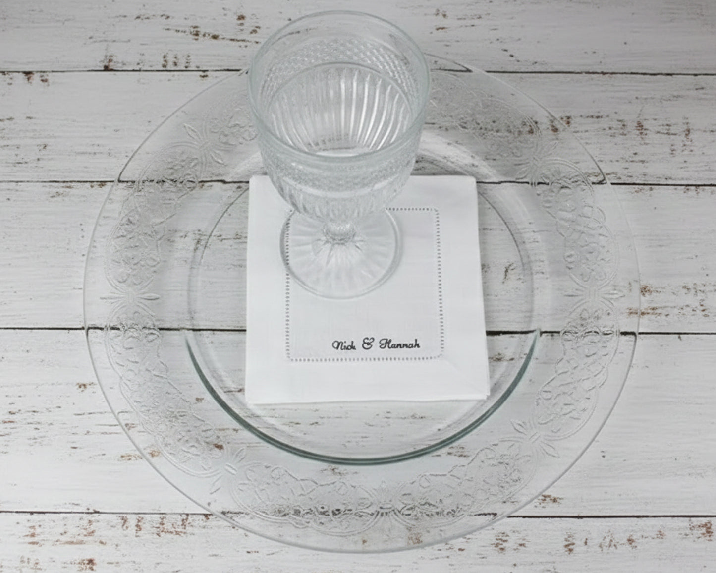 A premium white 100% linen hemstitch napkin featuring "Nick & Hannah" personalized script embroidery under a clear water glass.