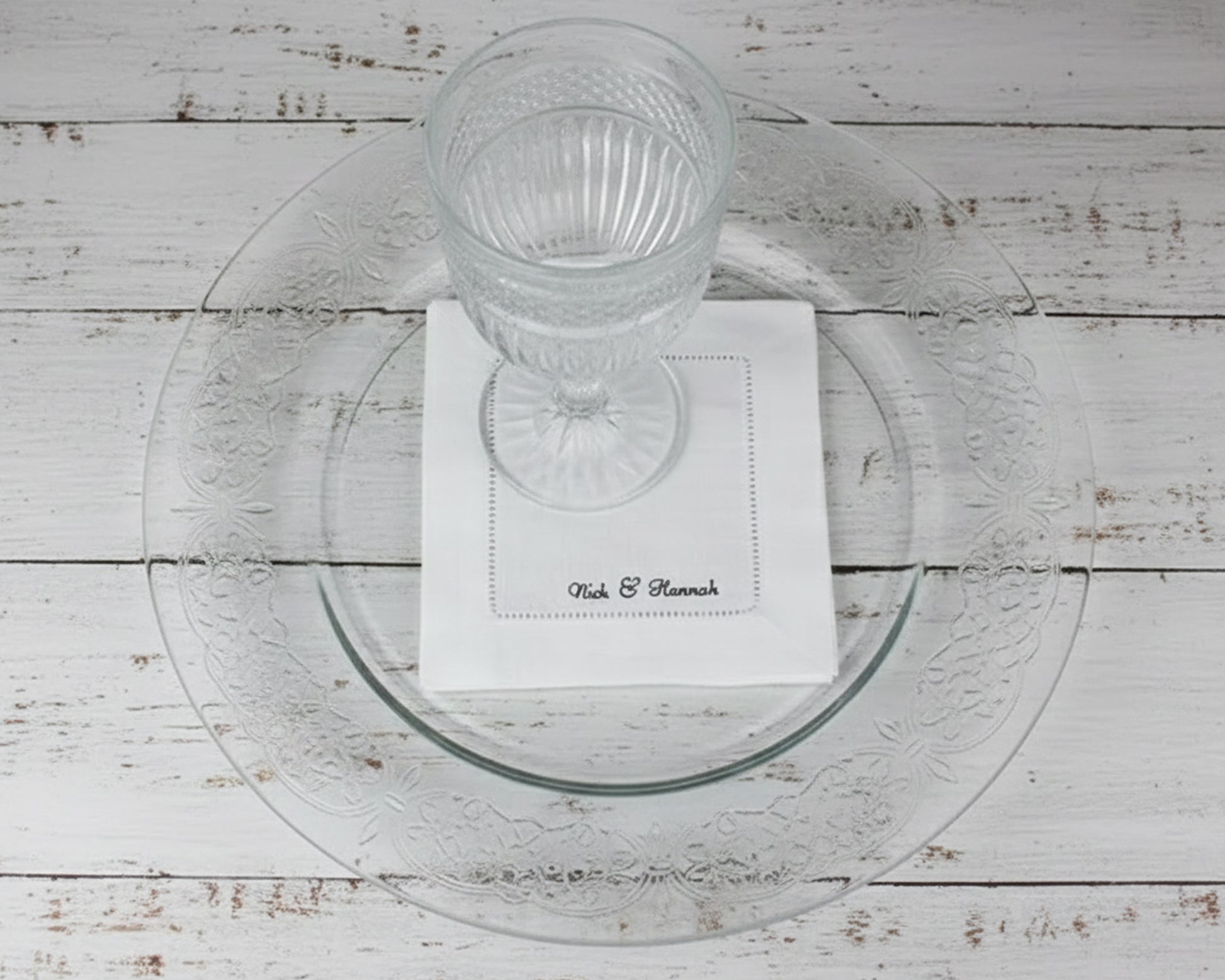 A premium white 100% linen hemstitch napkin featuring "Nick & Hannah" personalized script embroidery under a clear water glass.