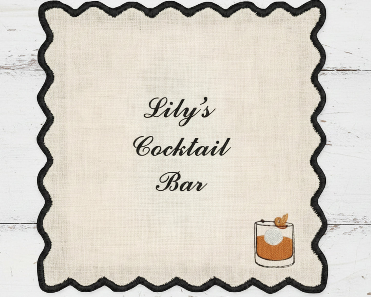 A premium white cotton bar napkin with a black scalloped edge, customized with "Lily's Cocktail Bar" and a detailed Old Fashioned glass icon.
