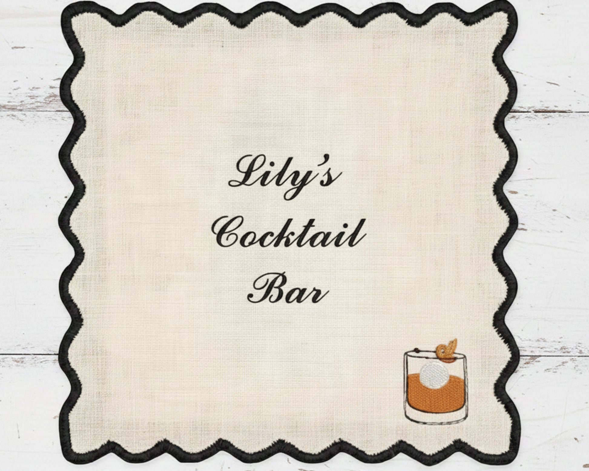 A premium white cotton bar napkin with a black scalloped edge, customized with "Lily's Cocktail Bar" and a detailed Old Fashioned glass icon.
