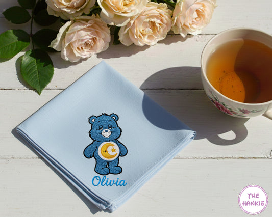 A soft sky blue cotton handkerchief personalized with the name "Olivia" and an embroidered blue Bedtime Bear character.
