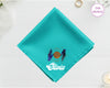 A radiant turquoise cotton pocket square featuring the name "Olivia" below a celestial indigo and gold Gemini twin hands icon.