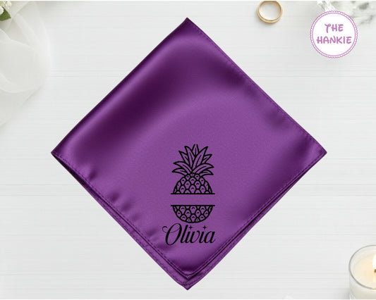 A royal purple luxury satin handkerchief personalized with the name "Olivia" below a black-threaded split-monogram pineapple design.