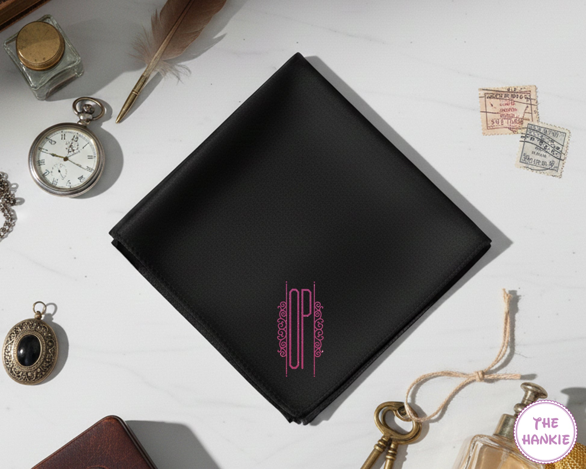 A sleek black cotton pocket square with personalized pink vinyl initials "OP" enclosed in a decorative modern geometric frame.