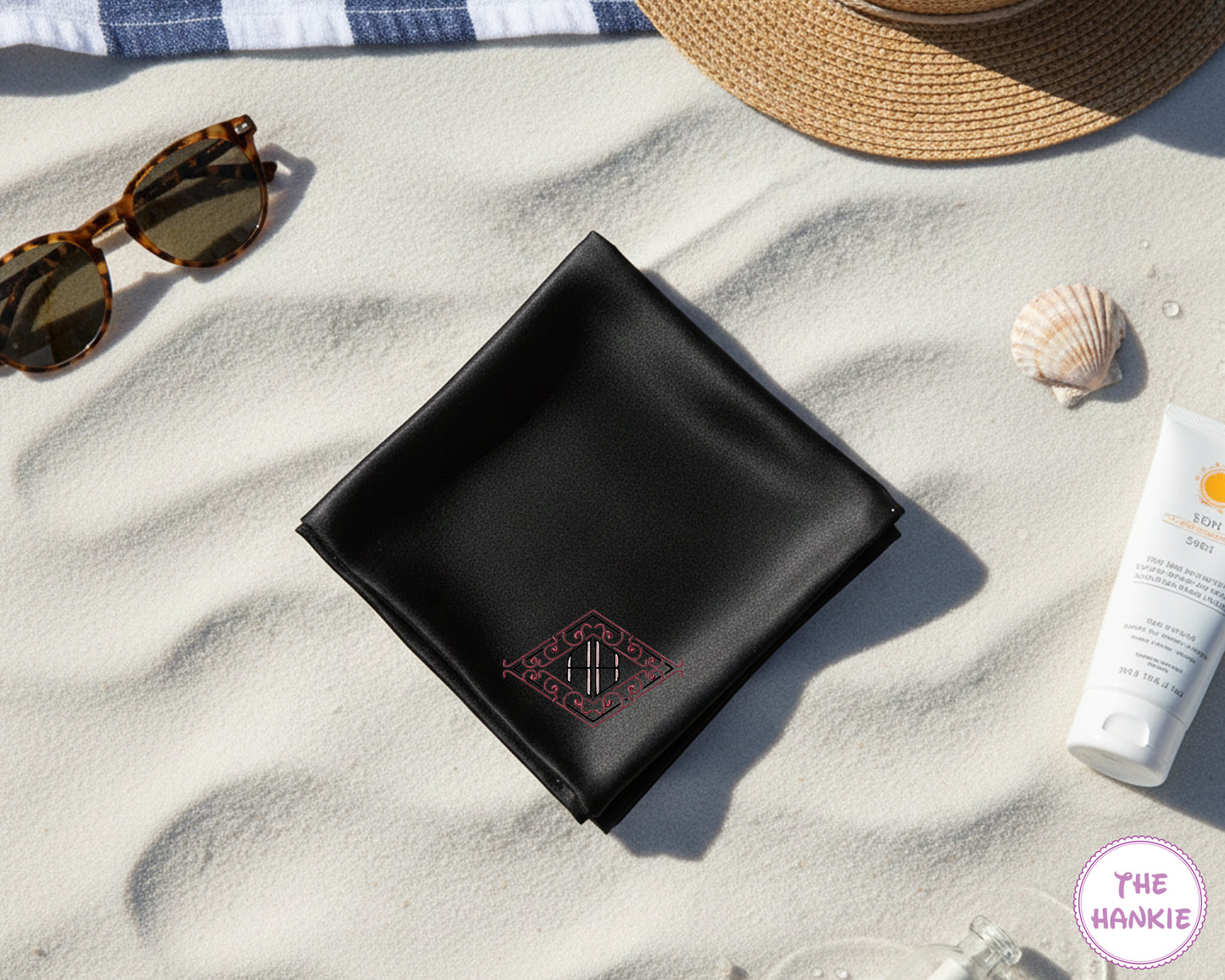 A premium black satin pocket square featuring a personalized pink interlocking script monogram on a tropical beach background.