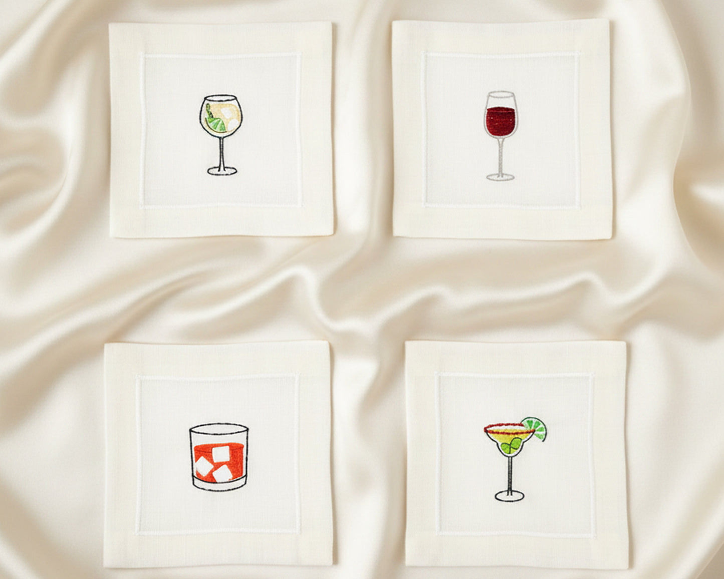 Close-up of four cotton napkins with colorful embroidery including an Aperol Spritz, Blue Margarita, Martini, and Espresso Martini.