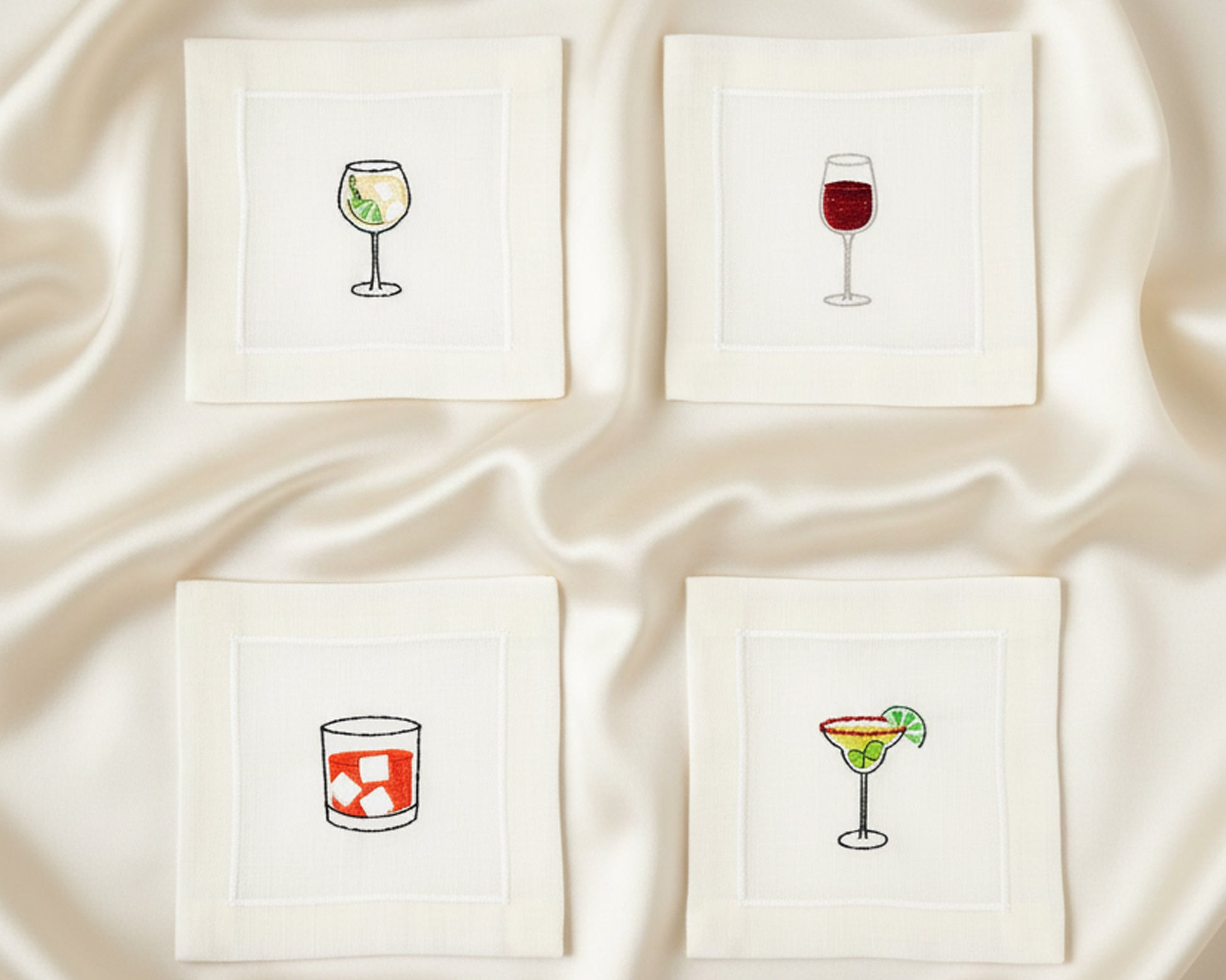 Close-up of four cotton napkins with colorful embroidery including an Aperol Spritz, Blue Margarita, Martini, and Espresso Martini.