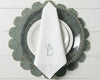 Elegant table setting featuring a white monogrammed napkin with sage green initials on a leaf-shaped charger plate