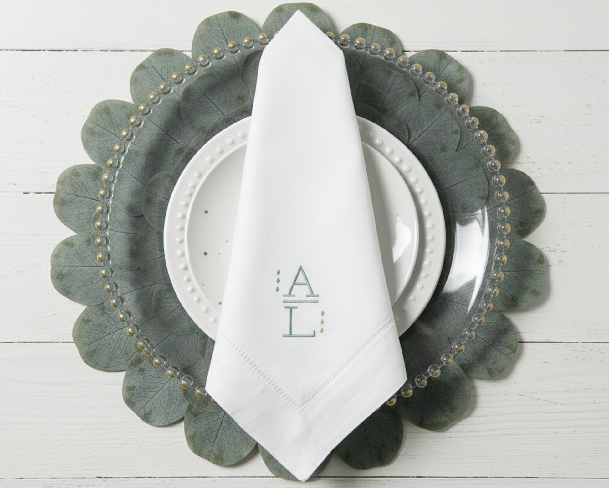 Elegant table setting featuring a white monogrammed napkin with sage green initials on a leaf-shaped charger plate