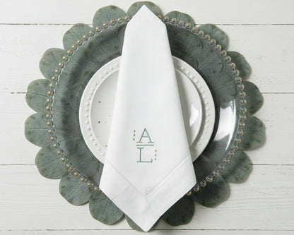Elegant table setting featuring a white monogrammed napkin with sage green initials on a leaf-shaped charger plate