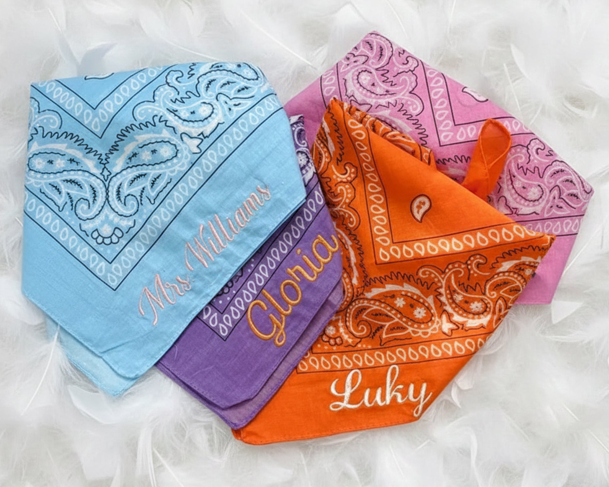 Folded personalized bachelorette bandanas with script embroidery displayed on a soft white feather background