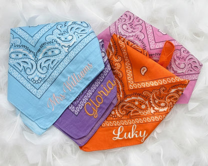 Folded personalized bachelorette bandanas with script embroidery displayed on a soft white feather background