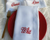 White napkins with red names embroidered on them, placed on a red plate with a gold fork.