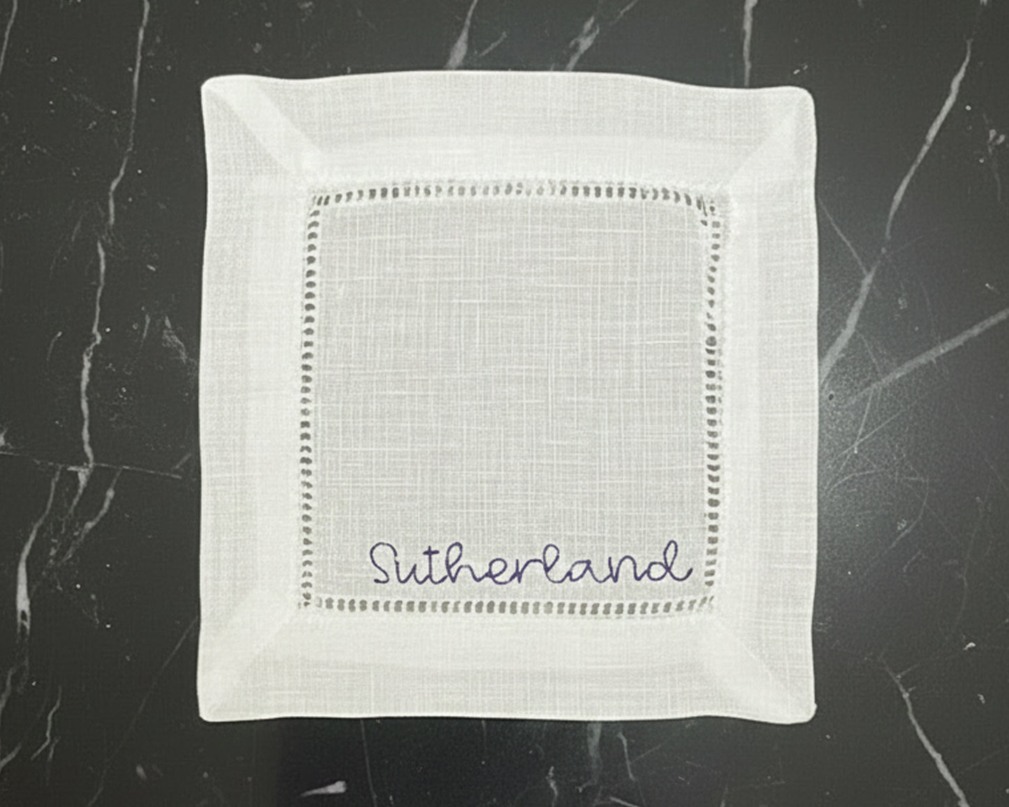 A stack of three crisp white hemstitch napkins, each featuring a different personalized monogram in a high-density navy blue thread.