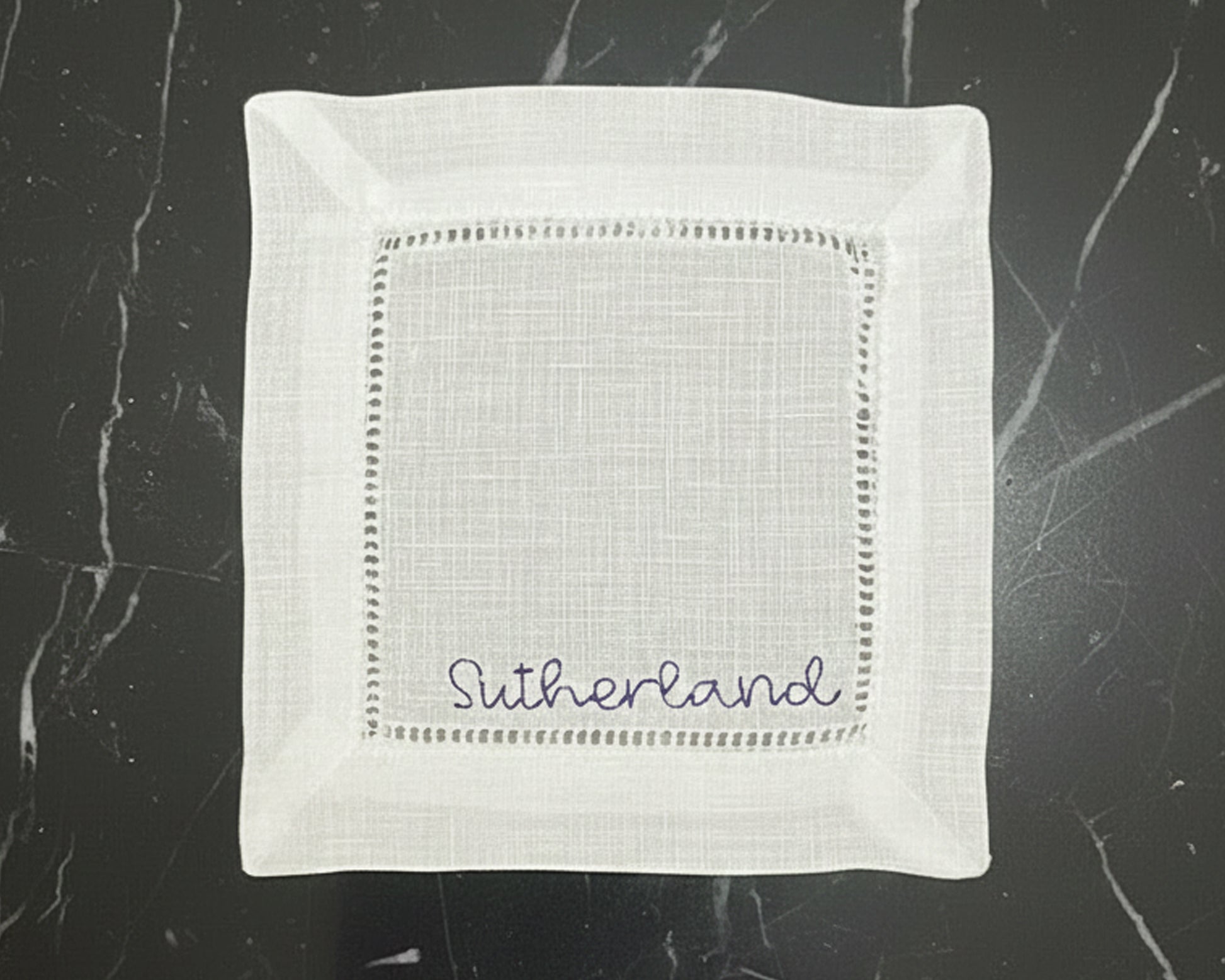 A stack of three crisp white hemstitch napkins, each featuring a different personalized monogram in a high-density navy blue thread.