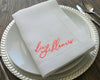 Close-up detail of vibrant coral script embroidery on a white linen napkin showing the "die Schlömers" text and satin stitching