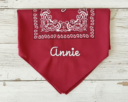Four folded bandanas in red, cream, black, and light blue showcasing different custom name embroidery styles