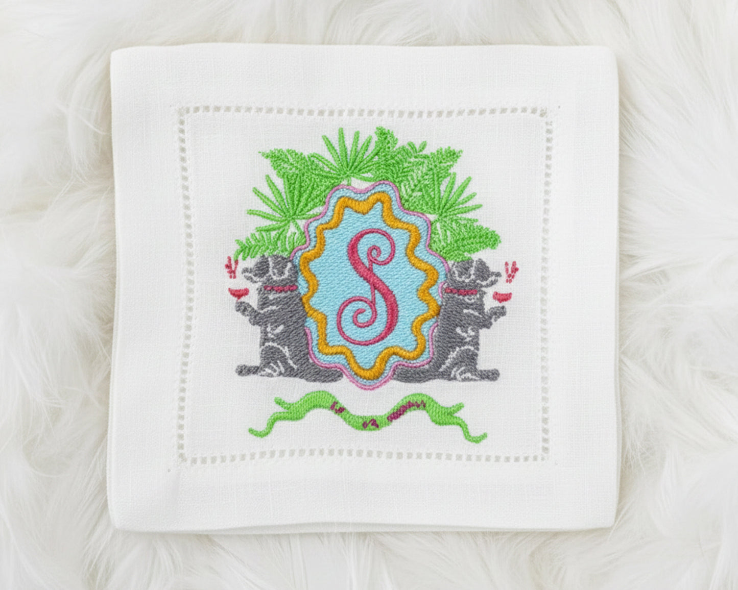 Custom embroidered napkin with a whimsical crest featuring dog motifs and a red 'S' initial