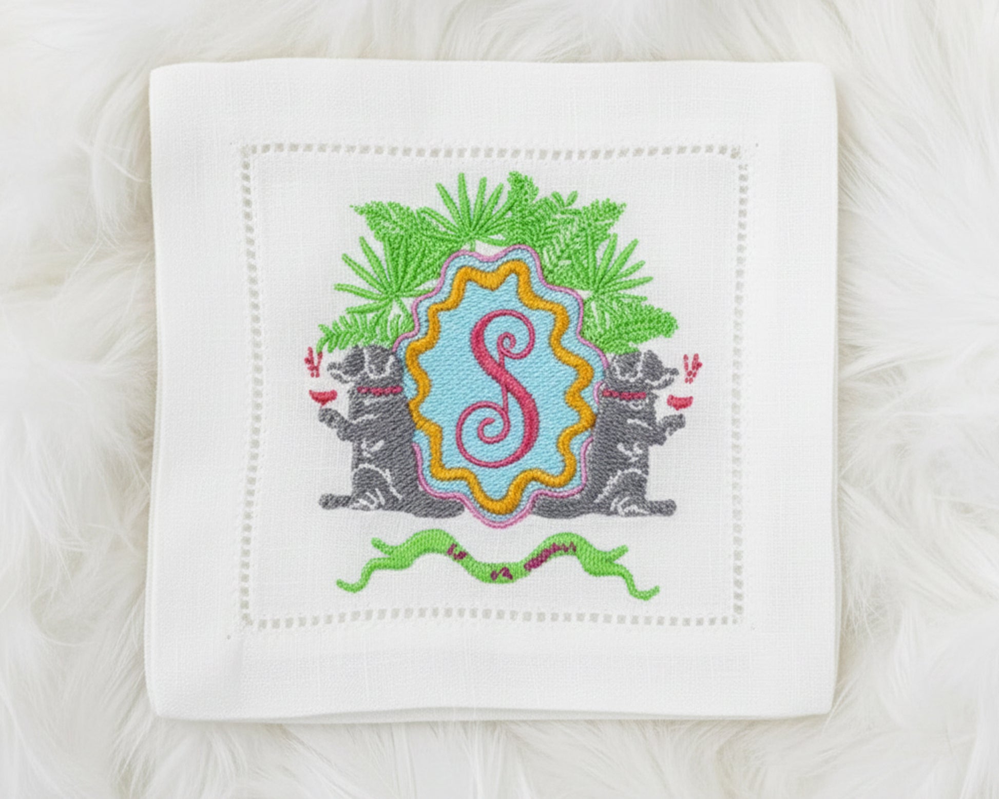 Custom embroidered napkin with a whimsical crest featuring dog motifs and a red 'S' initial