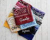 A stack of colorful paisley bandanas in red, blue, black, and pink featuring personalized names like Annie, Charlotte, and Olivia in chain stitch embroidery