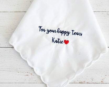 A white scalloped-edge wedding handkerchief made of 100% cotton, featuring navy blue embroidery that reads "For your happy tears Katie" with a small red heart.