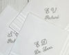 Close-up of three white cotton keepsake handkerchiefs with personalized grey embroidered monograms and script names like "Richard" and "De Leon".